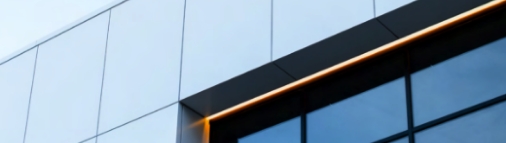Close-up of a modern glass building facade with reflective windows and a sleek black frame accented by a thin, glowing orange light strip.