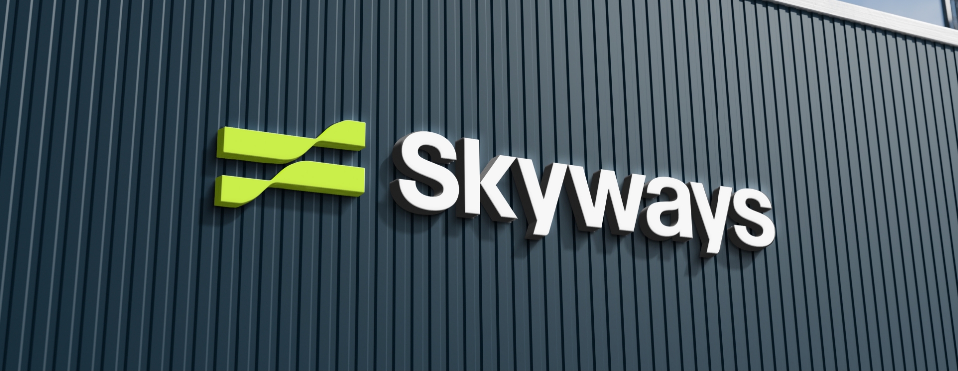 The image shows a modern building facade with the word Skyways in large white letters next to a green abstract logo, all mounted on dark vertical metal panels.