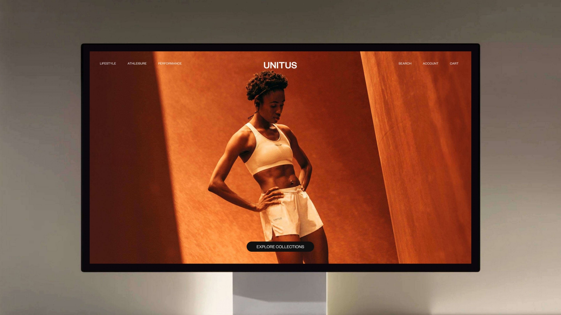 A computer monitor displays a website featuring a woman in athletic wear standing confidently against a warm, orange background, with the brand name UNITUS and navigation options at the top.