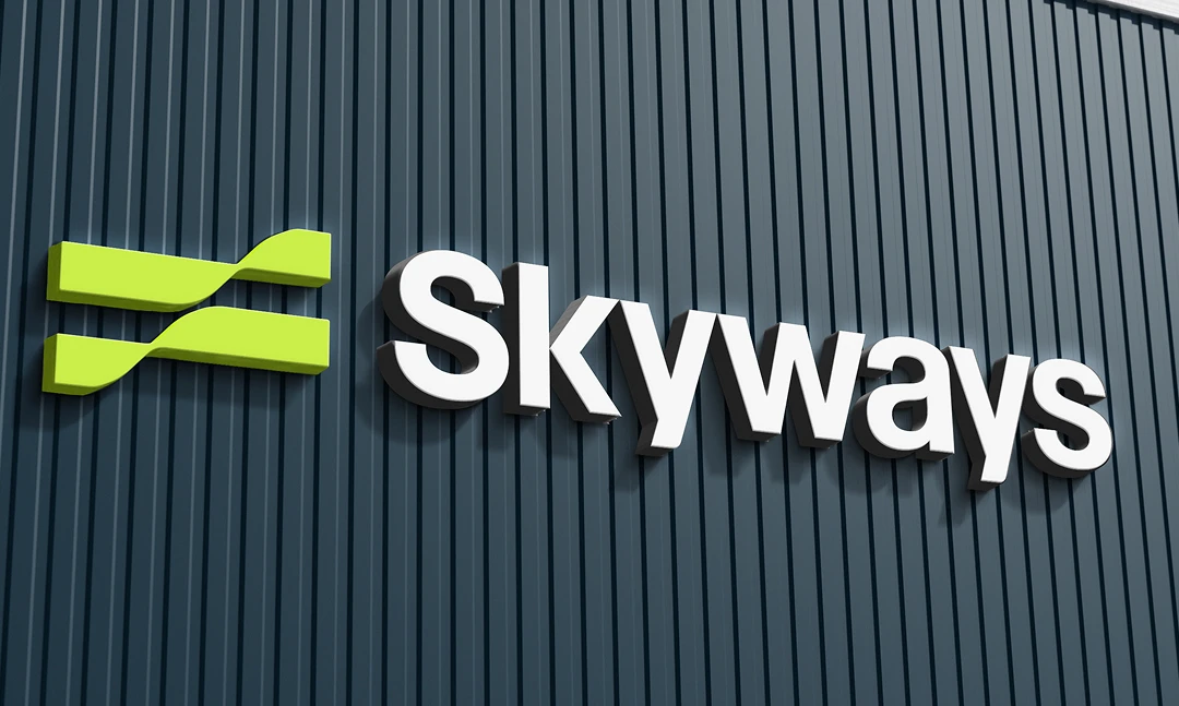 The Skyways logo is displayed on a dark blue corrugated wall, featuring bold white letters and a green abstract symbol to the left of the text.