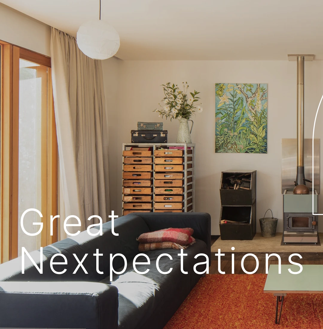 A cozy living room with a dark blue sofa, stacked wooden crates, a wood-burning stove, a green coffee table, and a painting on the wall. Text reads Great Nextexpectations in white letters.