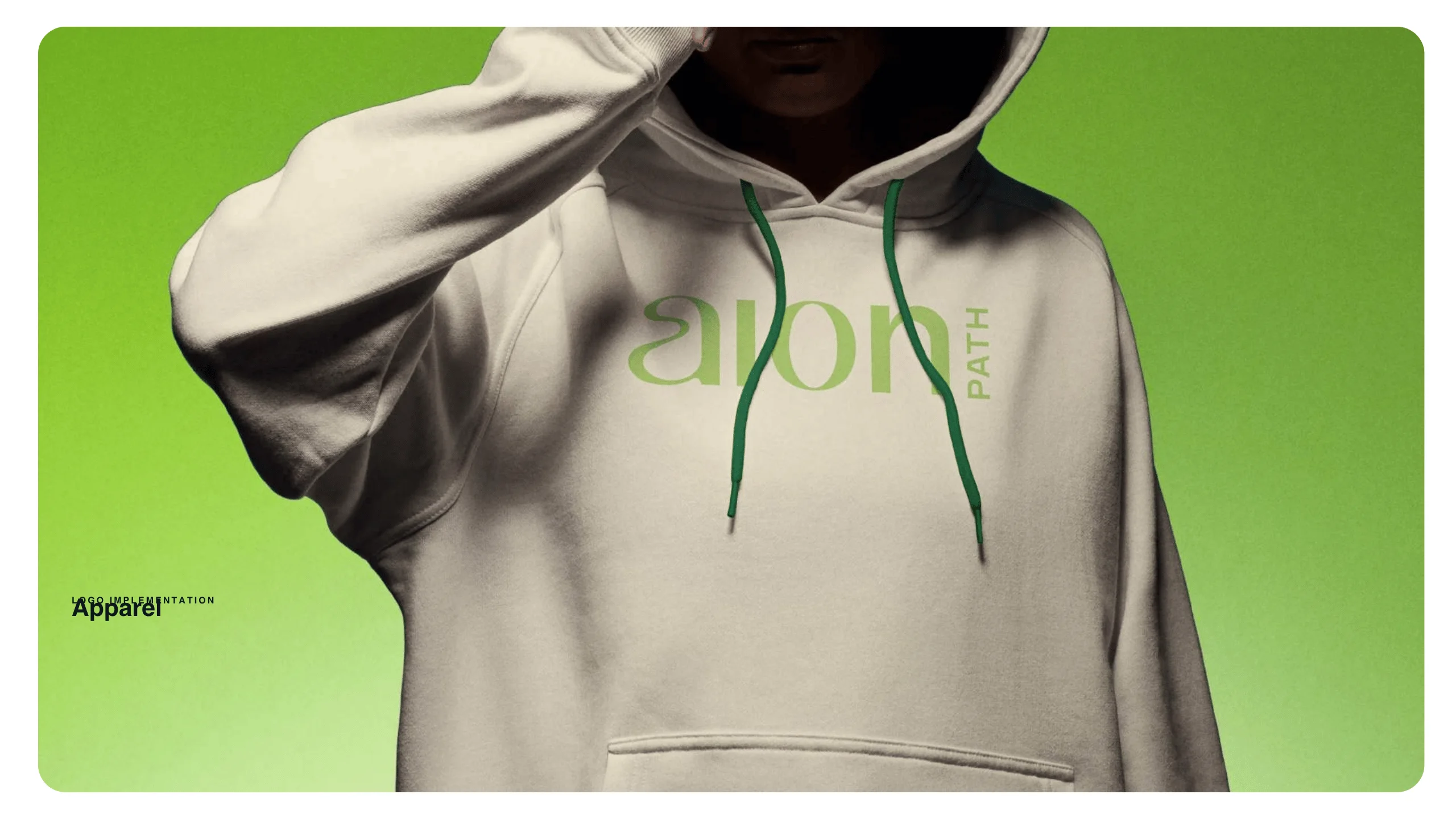 A person wearing a white hoodie with green drawstrings and the word aion PATH printed in green, standing against a gradient green background. The person’s face is partly obscured by the hoodie.