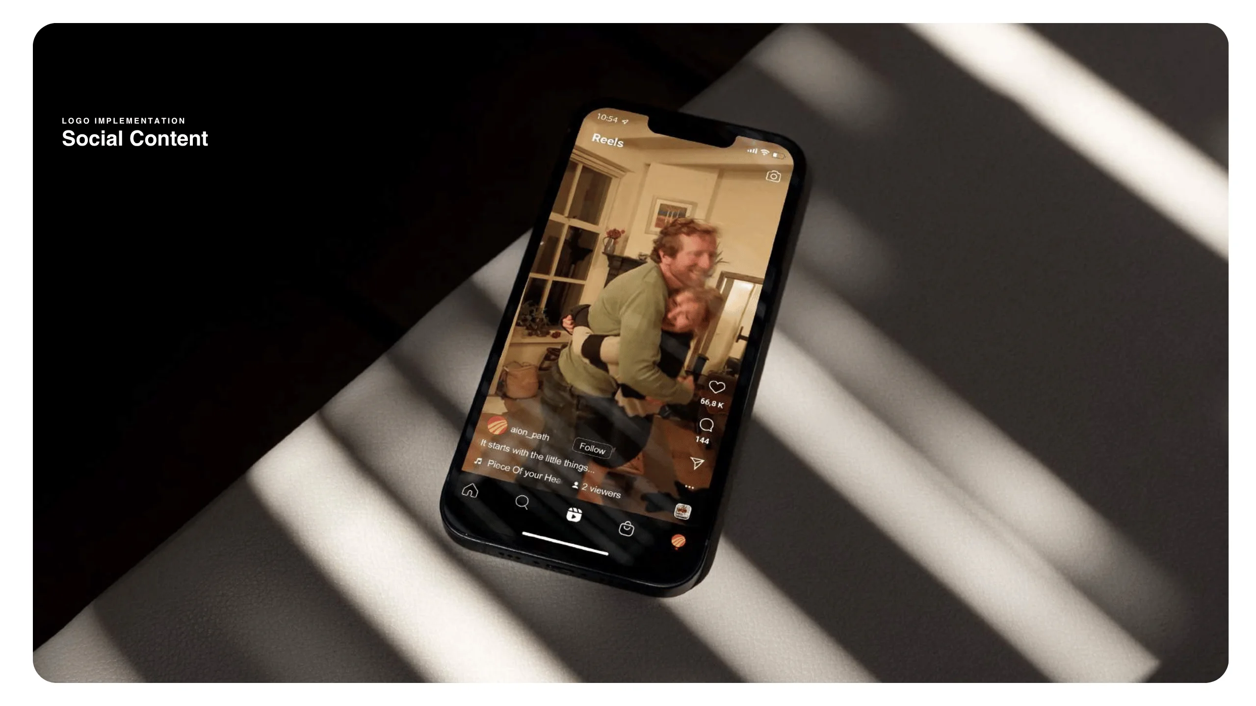 A smartphone on a couch displays a social media reel of two people dancing playfully in a living room, with sunlight casting striped shadows across the scene.