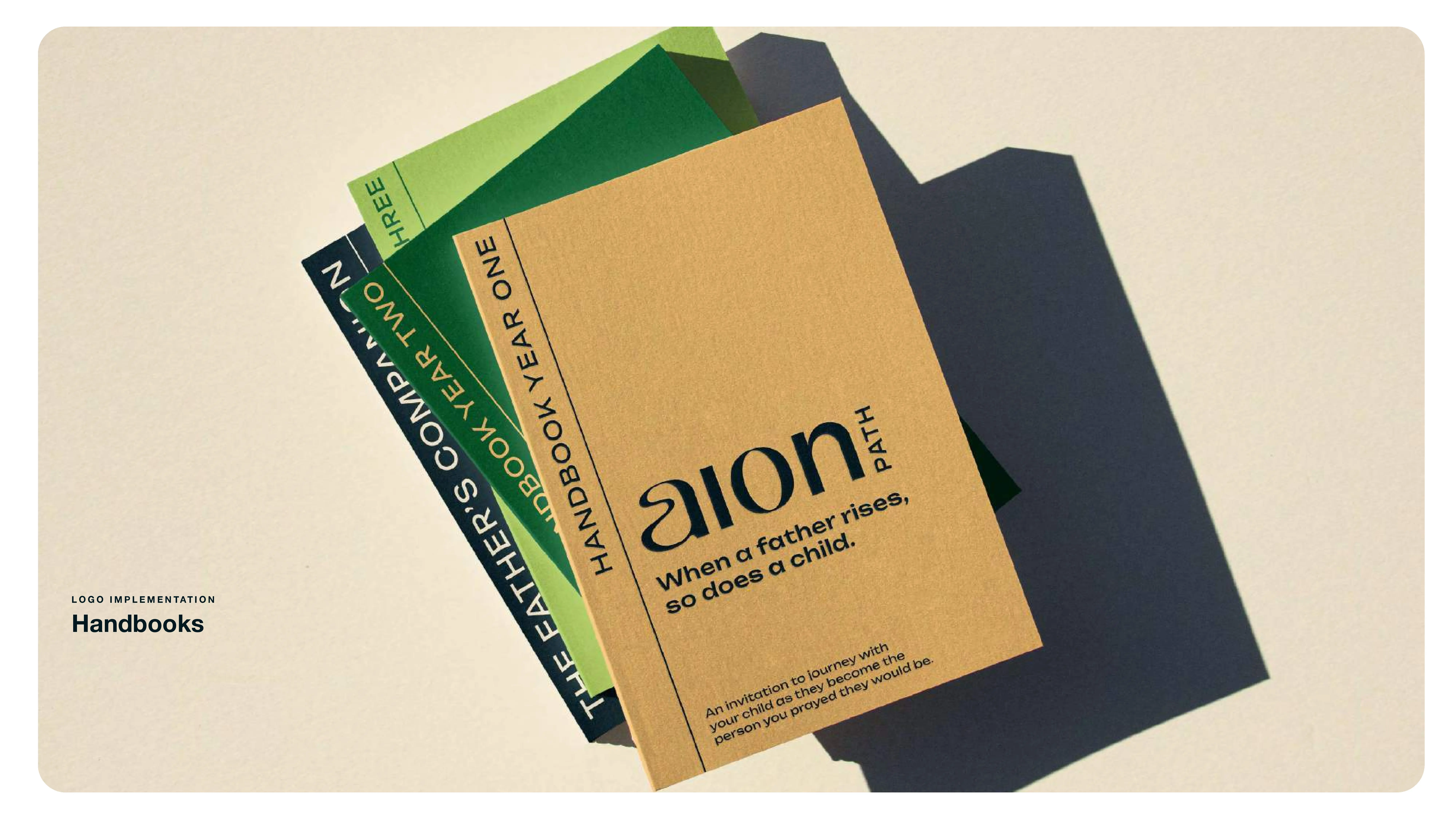 Three handbooks stacked on a light surface; the top one is labeled “Aion Path: When a father rises, so does a child,” with two green books underneath titled “Handbook Year One” and “Handbook Year Two.”.