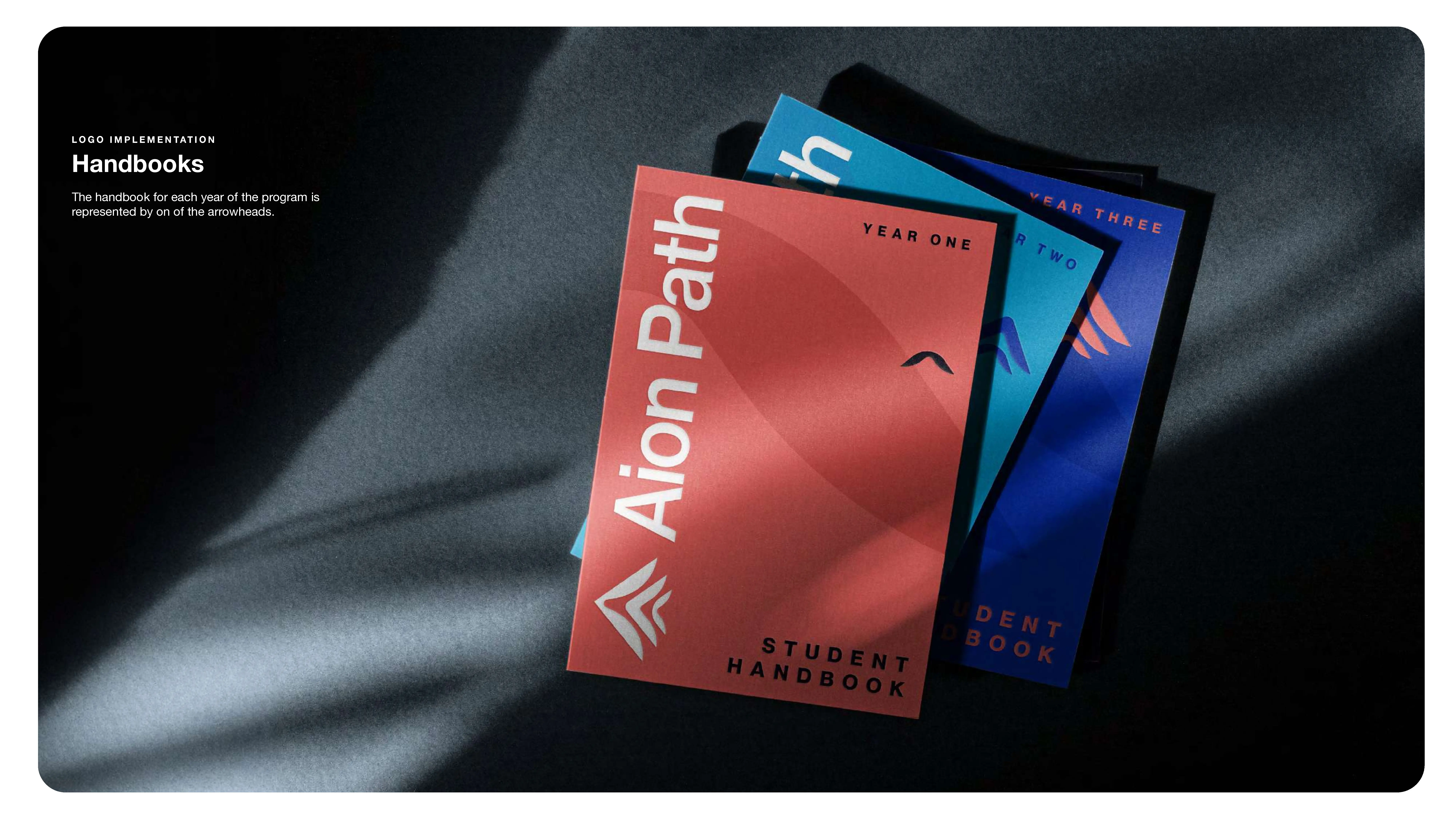 Three colorful student handbooks labeled Aion Path for different years are arranged on a dark surface with dramatic diagonal lighting and shadows. Text on the left describes the handbooks and their purpose in the program.
